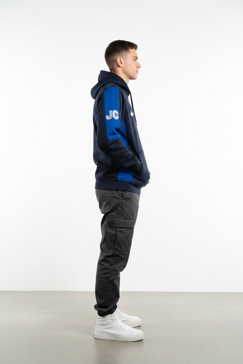 A navy blue and bright blue athletic jacket hanging on a hook inside a doorway. The jacket features a white 'JC' logo and a white swoosh on the sleeve.