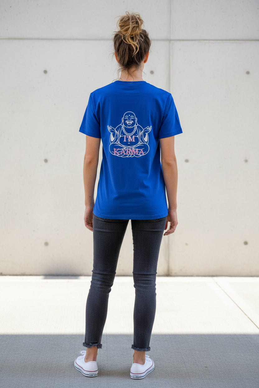 A royal blue short-sleeve t-shirt hanging on a black hanger in front of a glass door, featuring a white graphic of a meditating Buddha with the text 'I'M KARMA' on the front.