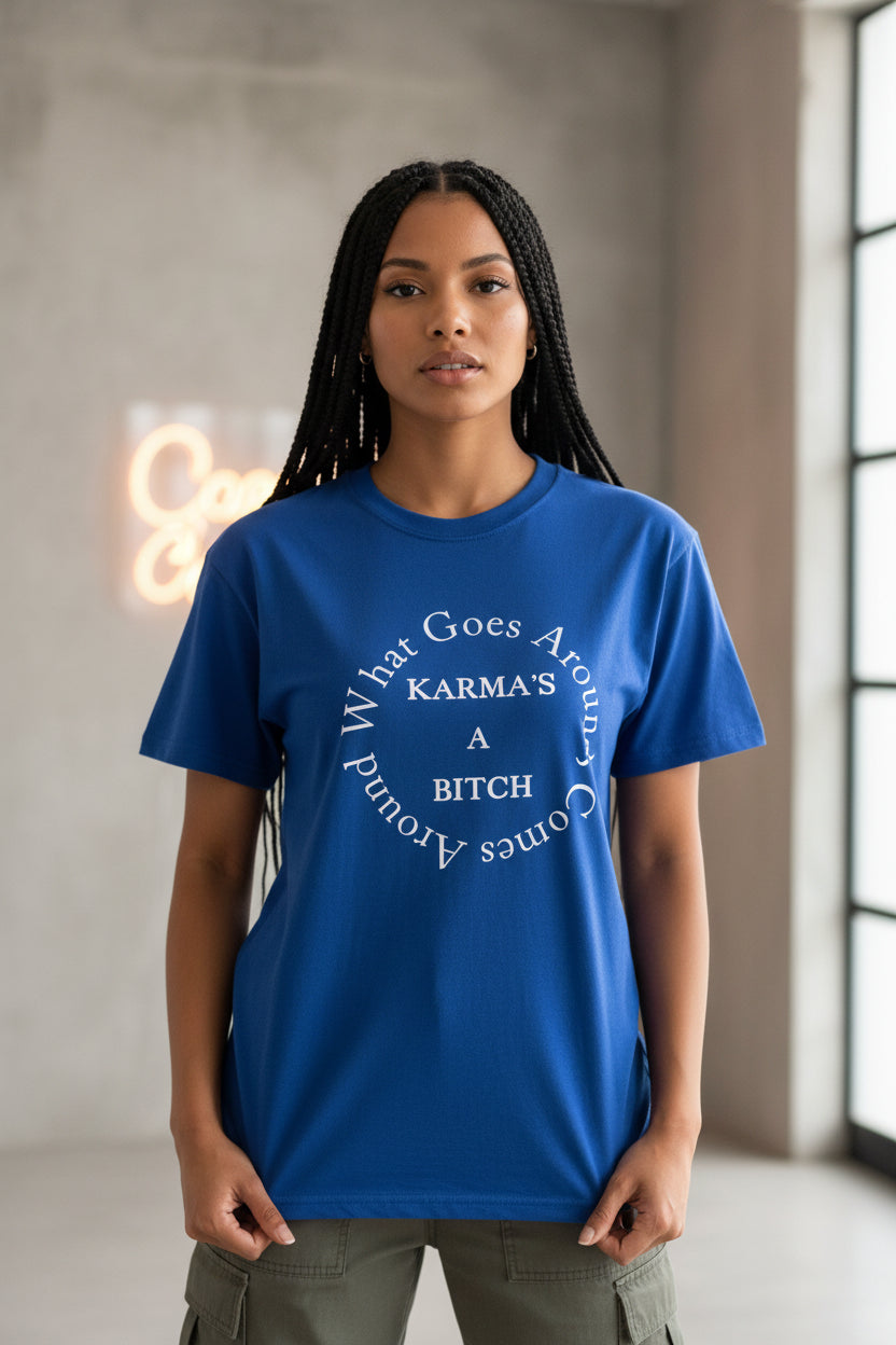 A royal blue short-sleeve t-shirt hanging on a black hanger in front of a window. The shirt features a white circular graphic print on the chest that reads 'What Goes Around Comes Around' with 'KARMA'S A BITCH' in the center.